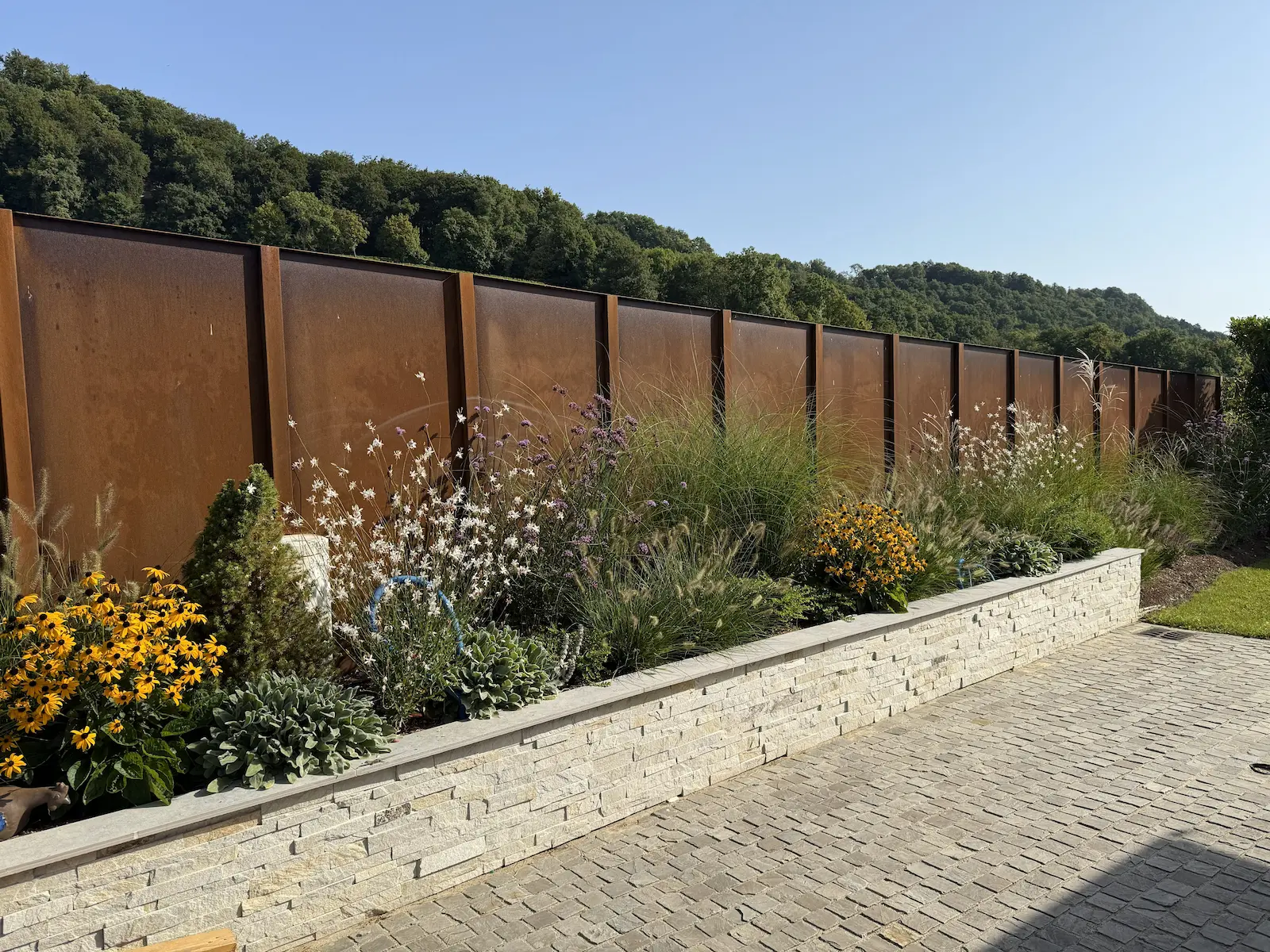 Aménagement de massif paysager contemporain avec graminées et vivaces, muret en pierre et clôture en acier corten, réalisé par un paysagiste à Genève.